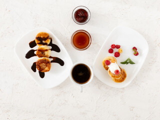 Cup of coffee and curd fritters with sour cream, berries and chocolate on the porcelain plates.