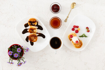 Cup of coffee and curd fritters with sour cream, berries and chocolate on the porcelain plates.