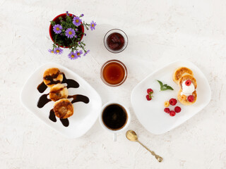 Cup of coffee and curd fritters with sour cream, berries and chocolate on the porcelain plates.