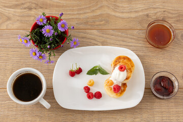 Cup of coffee and curd fritters with sour cream and berries on the porcelain plates.