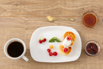 Cup of coffee and curd fritters with sour cream and berries on the porcelain plates.