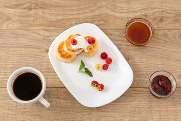 Cup of coffee and curd fritters with sour cream and berries on the porcelain plates.