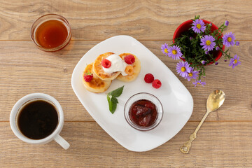 Cup of coffee and curd fritters with sour cream and berries on the porcelain plates.