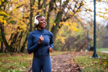 Ecstatic jogger runs on running trail of fallen leaves, with golden and green trees creating a serene, seasonal backdrop.