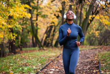 Happy woman jogs along a leaf-covered forest trail, surrounded by warm autumn colors and tall trees as she enjoys an outdoor run.