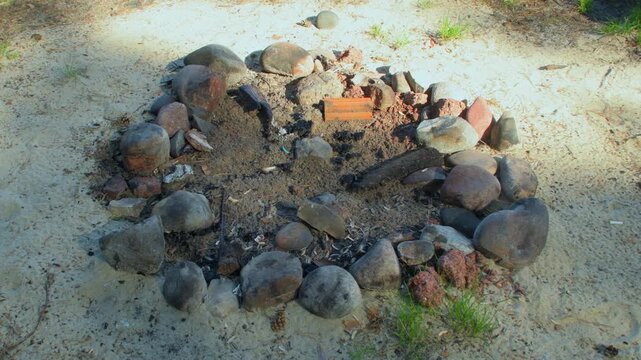 A place with an extinguished campfire on the seashore. A fire pit lined with sea pebbles. A campsite with old bonfire for tourists.