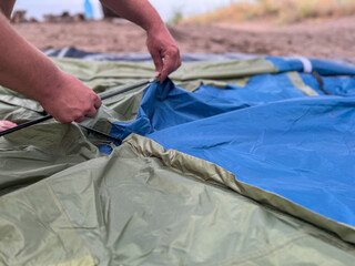Man's hands assembling tent on ground for camping