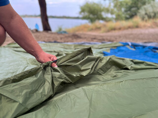 Person pitching tent outdoors near lake for camping