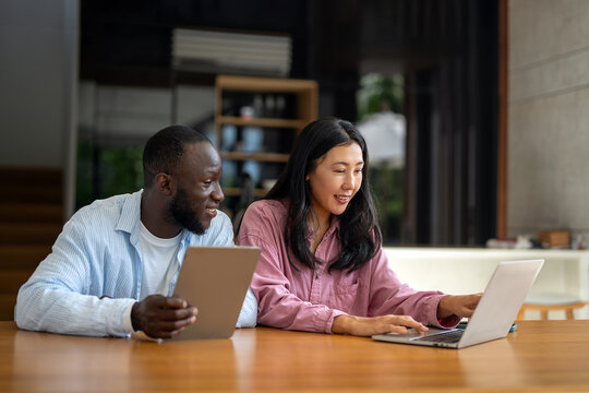 Business team, two happy diverse, multiethnic executives working together using laptop in office. - Powered by Adobe