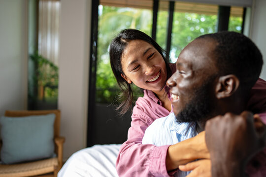 Young diverse couple joyfully smiling together in their bright living room, wearing casual clothes