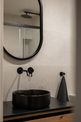 Modern bathroom interior with a round mirror, black sink, and stylish faucet. Minimalist design with neutral tones and wooden accents.