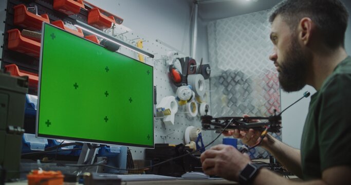 Engineer Using Green Screen For 3D Modeling And Design Software. Engineer Engrossed In Physical Assembly Of Drone While Utilizing Monitor With Green Screen For 3D Modeling, Flight Simulation Software.