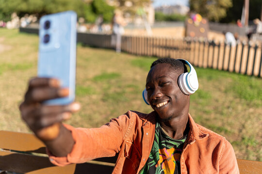 Young man smiling, taking a selfie outdoors, listening to music, having fun on his trip