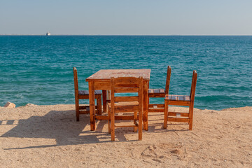 Wooden table and chairs on a beach by the Mediterranean Sea.