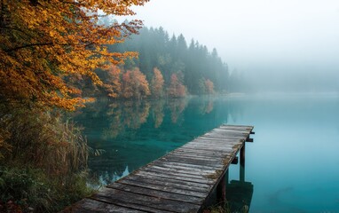 Naklejka premium Scenic autumnal lake view with a wooden dock, vibrant foliage, and a misty forest backdrop