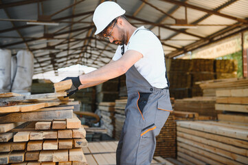 Carpenter stacking wooden planks in lumber warehouse