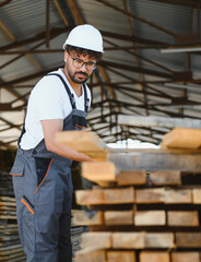 Carpenter arranging wooden planks in timber warehouse