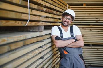 Arab carpenter smiling with crossed arms leaning on lumber in warehouse