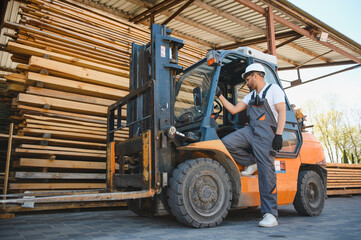 Warehouse worker stepping down from forklift near lumber stacks