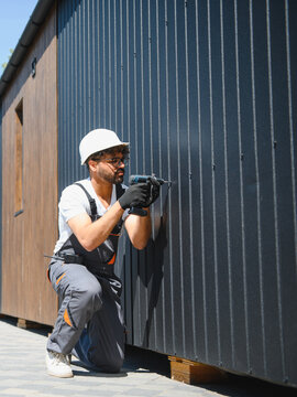 Construction worker using cordless drill installing metal siding on prefabricated building