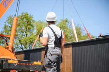 Obraz premium Construction worker supervising lifting of modular house onto truck