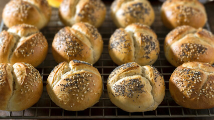 Delicious kaiser rolls with poppy and sesame seeds displayed fresh out of the oven on a cooling rack
