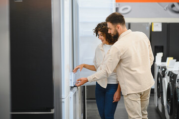 Fototapeta premium Couple choosing refrigerator in electronics store, examining home appliances before purchase
