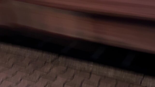 A motion-blurred, low-angle shot showing a train's wheels moving quickly over the railway track and sleepers upon arriving at a station platform. The scene depicts travel and transportation.