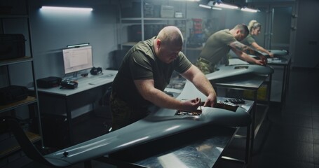 Installing Flight Electronics Technician Working on UAVs Core. Team in Uniform Installing or Checking Complex Flight Electronics Inside Body of UAV. Precision Required For Military Drone Systems.