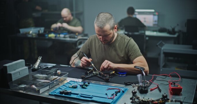 Technician Soldering Components on FPV Drone Circuit Board. Man Carefully Soldering Tiny Electronic Components Onto Small Circuit Board, Part of Drone. Precise Electronic Assembly in Modern Workshop.