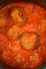 A top-down, zoomed-in view shows a cluster of large, cooked meatballs submerged in a thick, rich, red tomato sauce inside a metal pot
