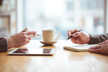 Senior businessman mentoring young employee during relaxed meeting at cafe table with coffee cup digital tablet and notebook sharing advice and guidance