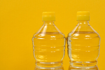 Two clear plastic bottles filled with light yellow liquid, likely sunflower oil, stand against a bright yellow background