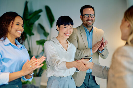 Business team celebrating a new partnership or successful deal, with two women shaking hands and colleagues clapping