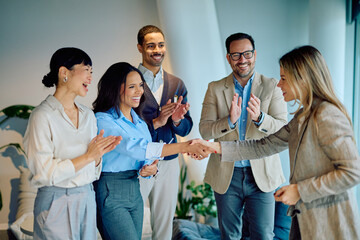 Diverse business team cheering achievement, two women making a deal with a handshake, showing teamwork and partnership