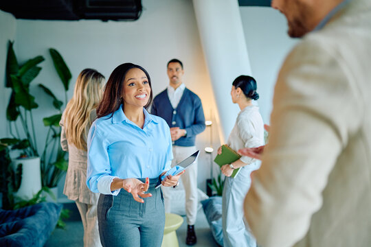 Multiracial business group conversing and interacting in an office lounge area. Woman holding a digital tablet and smiling