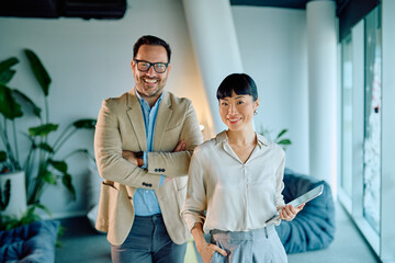 Two smiling diverse business people, a man and a woman, standing together in a bright, contemporary office, representing teamwork and success