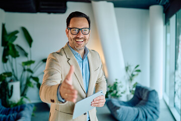 Smiling businessman holding a tablet, extending hand forward, offering a greeting, welcome, or partnership agreement