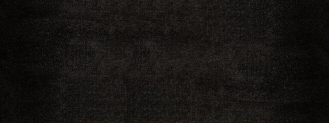 Wide, high-resolution texture of dark black or deep gray denim or twill fabric. Features a subtle diagonal weave pattern and minor natural fading, ideal for backgrounds and textile mockups