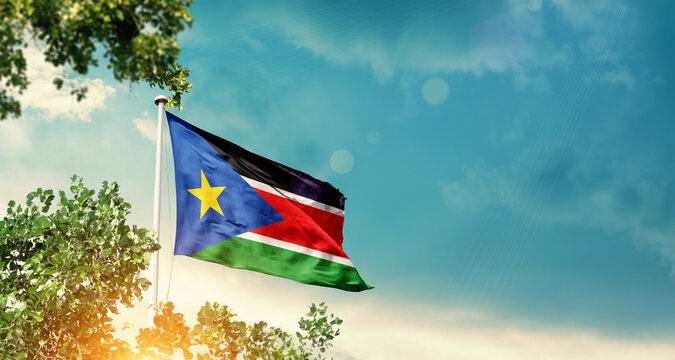 South Sudan national flag waving in the sky behind the tree. The flag blowing with beautiful sunlight. South Sudan national flag for independence day.