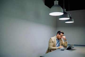 Businessman feeling exhausted and having a headache while working late on laptop, suffering from overwork and stress