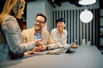 Diverse business team collaborating and smiling during a workplace discussion with a laptop device on the table