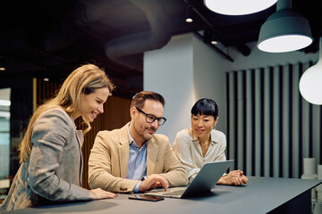 Diverse business professionals collaborating, working together on a laptop, sharing ideas and discussing strategy in a modern office