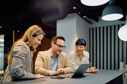 Diverse business professionals collaborating, working together on a laptop, sharing ideas and discussing strategy in a modern office