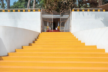 Yellow stairs to the villa. Wide stone staircase with white walls leads up to the house with garden