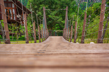 Low-angle close-up of a wooden suspension bridge surrounded by lush green forest. Natural adventure...