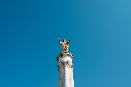 Golden statue of Jesus Christ with open arms on tall column at Sanctuary of Fatima, Portugal, viewed against deep blue sky, symbol of Christian faith, hope and blessing