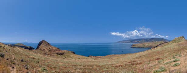 Panoramic coastal landscape of Ponta de Sao Lourenco Madeira, dry grassy slopes calm blue Atlantic water distant islands and mainland mountains