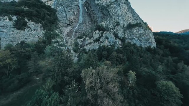 FPV drone and a bird flying near a massive waterfall n the Alps.