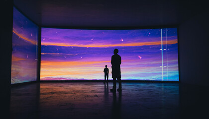 Two silhouettes gaze at an immersive digital art installation displaying a vibrant starry night sky with colorful clouds.